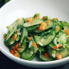 Chinese cucumber salad on the white plate. Asian cuisine. Bell pepper, cucumber and sesame seeds. Vegetarian dish. Toned photo.