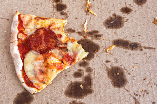 Leftovers of pizza in a takeaway box. An empty pizza box with one scrap of a piece remaining in the greased up cardboard container