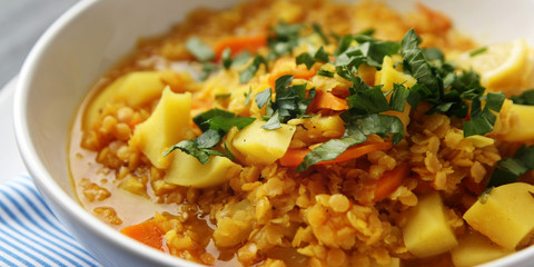 Red lentil stew with potato, carrot and turmeric. Toned photo. Healthy lunch on the round white plate. Colorful vegan dish with potato, carrot and turmeric. European cuisine. Vegetarian.