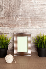Beautiful photo frame next to two pots of grass over vintage wooden background