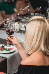 woman holds glass of red wine. people consider the color of the wine and try how it smells in different glasses