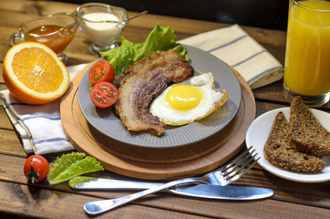 English Breakfast: fried egg with bacon, orange juice, tomatoes, zernovoi bread, lettuce leaf, top view.
