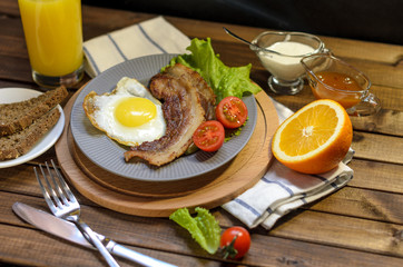 English Breakfast: fried egg with bacon, orange juice, tomatoes, zernovoi bread, lettuce leaf, top view.