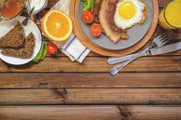 The concept of the English Breakfast: fried egg with bacon, orange juice and vegetables. Free space for text, top view.