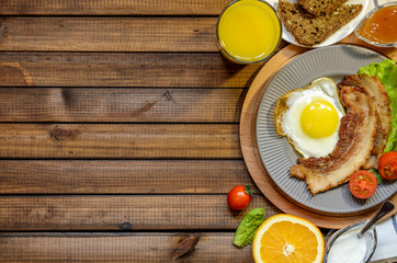 The concept of the English Breakfast: fried egg with bacon, orange juice and vegetables. Free space for text, top view.