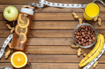 Healthy lifestyle; fitness bottle; fruits (oranges; apples and bananas); hazelnuts and peanuts; orange juice and measuring tape. Top view; the concept of free space for text