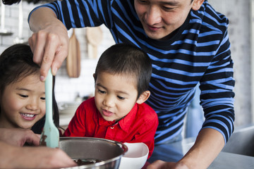 ボウルのチョコレートソースをヘラでかき集めるお父さん。息子と娘もお菓子作りに夢中。
