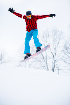 Picture of sports man in helmet with snowboard jumping in snowy resort