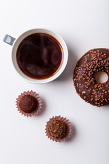 Chocolate donuts with cup of black coffee and sun glasses on brown background. Monochromatic concept.