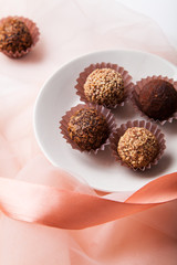 Variety of chocolate truffles with pink silk ribbon and transparent fabric on white background