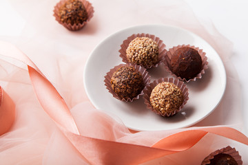 Variety of chocolate truffles with pink silk ribbon and transparent fabric on white background