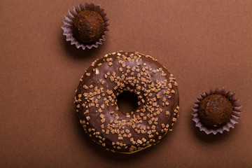 Chocolate donuts with chocolate truffles on brown background. Monochromatic concept.