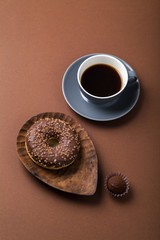 Chocolate donuts with truffles and cup of black coffee on brown background. Monochromatic concept.