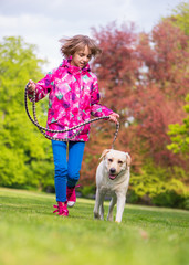 Little girl with labrador retriever on walk in park. Child is running on green grass with dog - outdoor in nature. Pet, domestic animal and people concept.