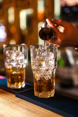 Close-up of expert bartender making cocktail in bar, splash of whiskey and rum.