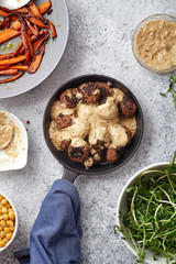 Flatlay with traditional swedish beef meatballs with gravy served in one portion black cast iron pan, handle wrapped in blue towel, plates with sauce, baked carrots and chickpeas. Dinner concept.