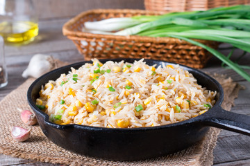 Asian fried rice with eggs and corn in a frying pan on wooden background