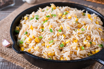 Asian fried rice with eggs and corn in a frying pan on wooden background