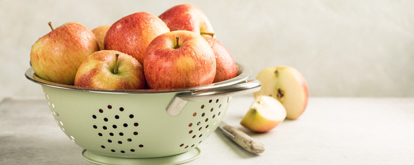 Fresh red apples in green metal strainer on light background. Healthy food concept with copy space. Banner.