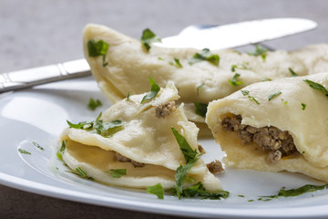 Pierogi, pyrohy or dumplings, filled with beef meat and covered with parsley on plate