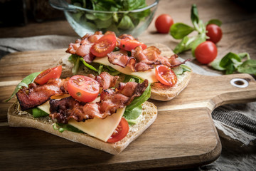 Ciabatta sandwich with arugula salad, bacon and yellow cheese.