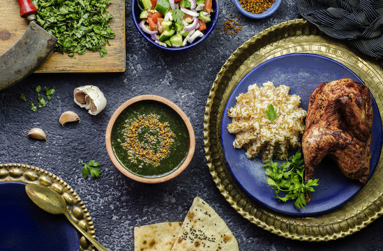 Arabic cuisine; Egyptian dish Molokhya or Molokhia placed with rice,chicken,pita bread,oriental green salad,crispy fried garlic and fresh ingredients on rustic background.