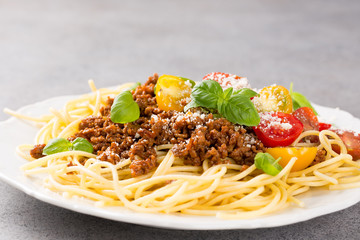 Rustic plate of tasty spaghetti Bolognaise topped with minced beef, grated parmesan cheese, cherry tomatoes and fresh basil. Copy space.