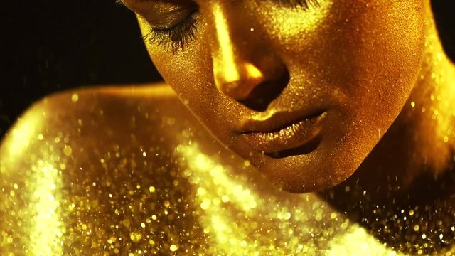 Fashion model woman in golden bright sparkles posing in studio, portrait of beautiful sexy girl with golden skin. Glitter gold metallic shine makeup. Slow motion 4K UHD video footage. 3840X2160