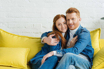 Embracing smiling couple sitting on sofa