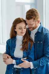 Redhead woman and man embracing by window