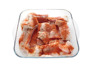 Many raw juicy sliced fresh fish fillets pink pieces well sprinkled with red pepper inside square transparent bowl are ready for baking front view closeup