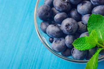 Fresh ripe blueberries with leaves in bowl on blue wooden planks