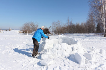 Man in a blue jacket building an igloo on a glade in the winter