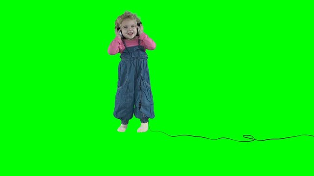 Adorable little girl child with big headphones dancing on green background