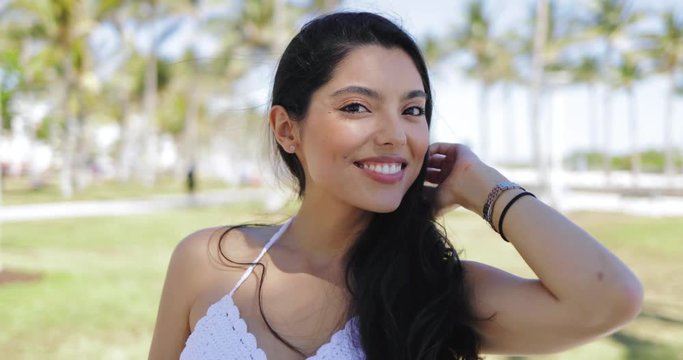 Portrait of beautiful ethnic brunette with long hair smiling at camera on background of tropical park. 