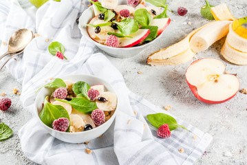 Healthy summer breakfast, fruit and berry salad with spinach, granola, apple and banana, white marble background