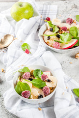 Healthy summer breakfast, fruit and berry salad with spinach, granola, apple and banana, white marble background