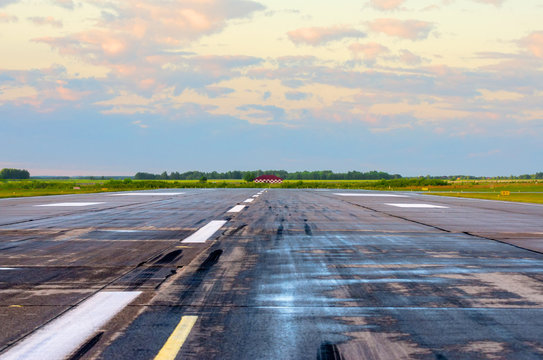 Sunrise with landscape airport of wet runway with traces of rubber tires on asphalt.