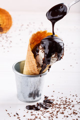 Homemade vanilla ice-cream with chocolate topping in waffle cone on white table.