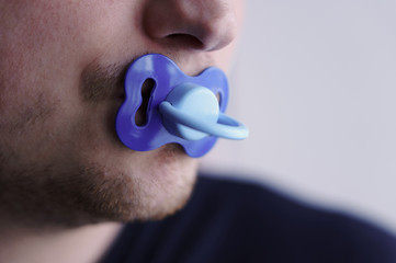 A young man holds a pacifier in his mouth