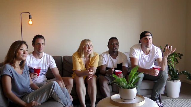 Group of young multinational adults watching TV. Slider shot