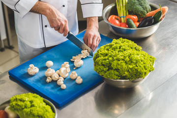 cropped image of chef cutting mushrooms at restaurant kitchen