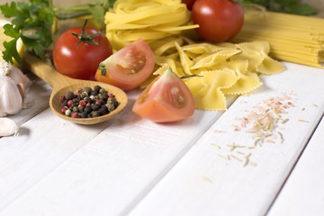 Dry pasta with vegetables on white wooden table.