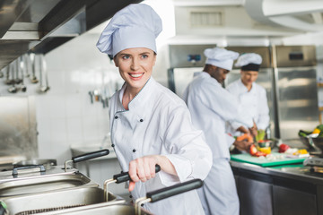 attractive chef frying food in oil at restaurant kitchen and looking away