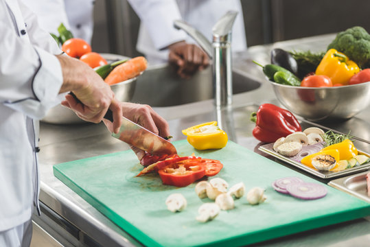 cropped image of chef cutting vegetables at restaurant kitchen
