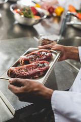 cropped image of african american chef holding tray with raw meat at restaurant kitchen