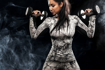 Sporty beautiful woman with dumbbells makes fitness exercising at black background to stay fit