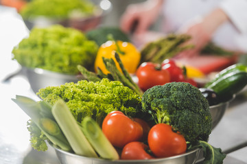 cropped image of chef cooking at restaurant kitchen with ripe vegetables on foreground