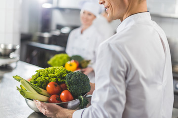 cropped image of chefs holding bowls with vegetables at restaurant kitchen