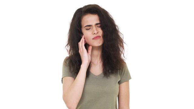 Portrait of hispanic woman with brown shaggy hair suffering from toothache touching cheek and expressing pain on face, over white background in studio. Concept of emotions